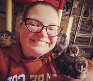 Jenn wearing an orange Cape Cod hoodie, wearing cat eye glasses, and sitting with two chick on one shoulder, one chick on the other, and a fourth chick on her arm.